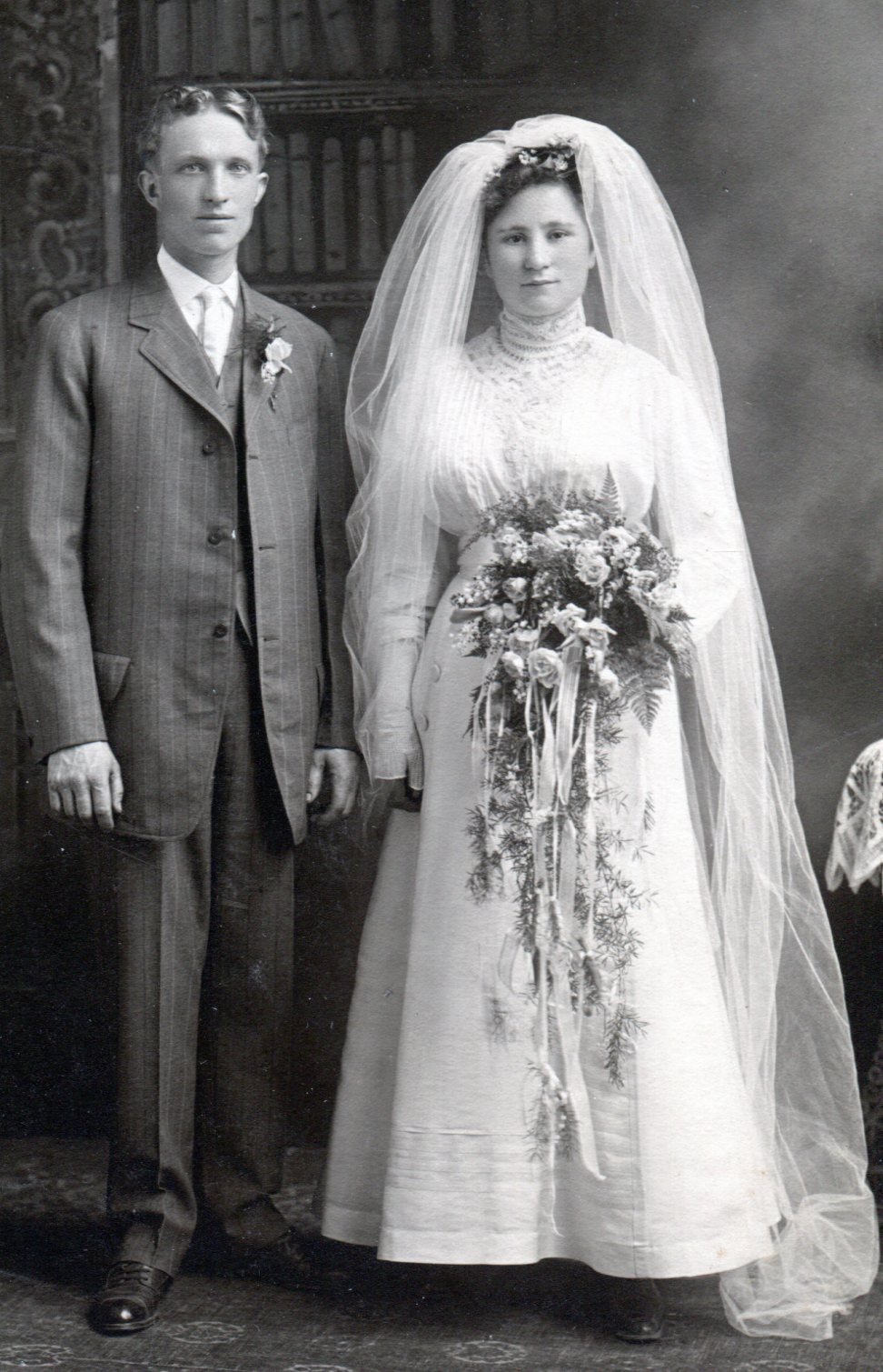 Bride and groom. Bride wears a white high neck dress, puffy bodice, and long skirt. 