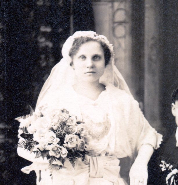 Close up of bride showing gathered veiling cap with veil attached at back and roses bouquet