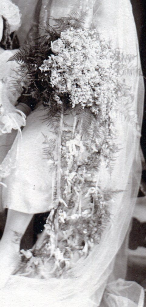 Bridal bouquet with many white flowers and small flowers tied to ribbons hanging down from bouquet.