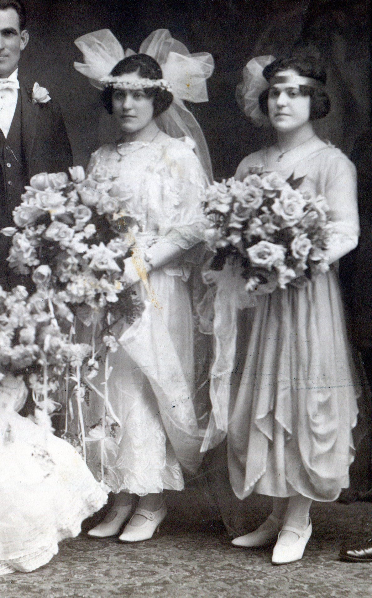 Bride and maid-of-honor in flowing ankle-length dresses and holding  large bouquets of roses.