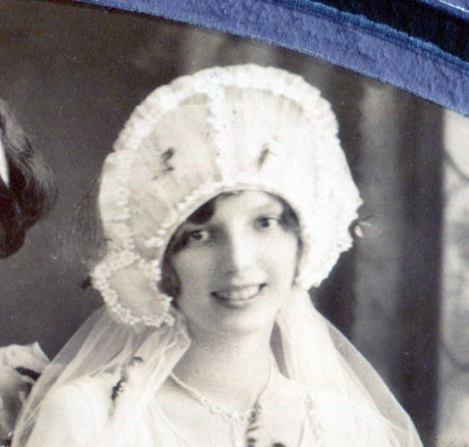 The bride's headpiece of a wire frame supporting a net fabric with lace edges frames her face.