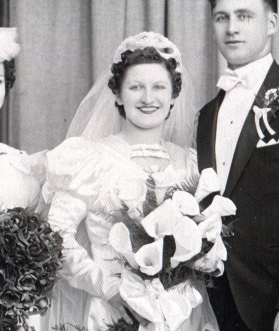 Close up of white satin bridal gown with puffy top of long sleeves, headdress of pearls on wire and Calla Lilies bouquet