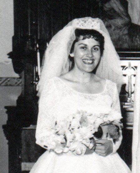 Smiling bride wearing a beaded crown headpiece and short veil and holding a bouquet of five orchids.