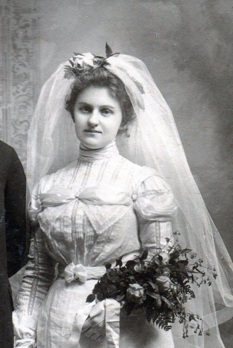 Bridal gown top with high neck collar, vertical flat lace bands and large flat bow across bodice.  