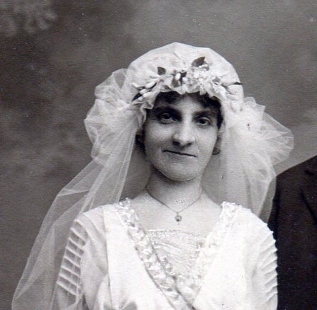 Bridal headpiece is puffy net cap of sheer fabric gathered to fit her head with wax flowers and puffs of veil netting on the sides.