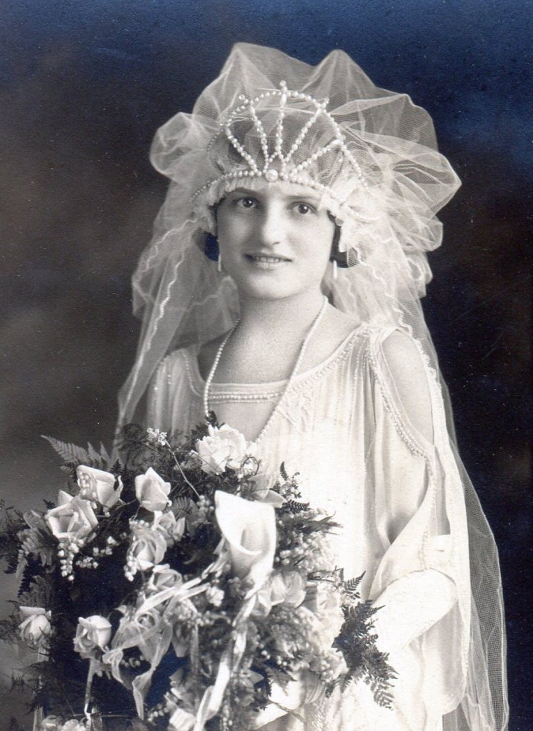 Bridal gown with scooped neckline and split sleeves trimmed with rows of small white beads.