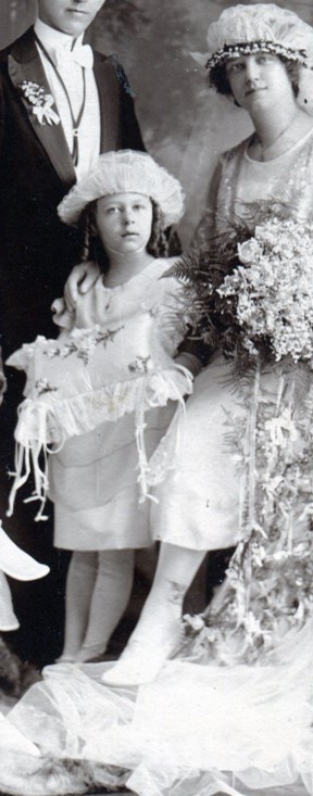 Little girl ring bearer holding satin pillow with ruffled edge and wearing a hat of stiffened netting with an up-turned brim.