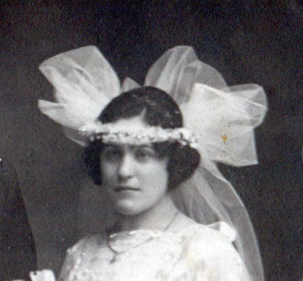 Bridal headpiece of small flowers in band around head with puffs of veil netting on back and sides.