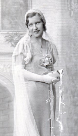 Close up of satin bridal gown with V-neck, short cap sleeves, fabric flower at base of V, and holding prayer book with ribbons.