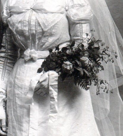 Bridal bouquet of six red roses and thin greenery tied with a white satin ribbon.