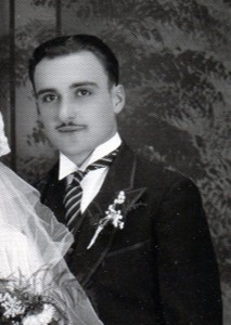 Groom has thin moustach, stiff stand up collar and small boutonniere of small white flowers.
