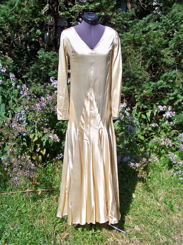 A cream satin wedding gown with a straight cylinder shape, long sleeves, and slightly flaring skirt.