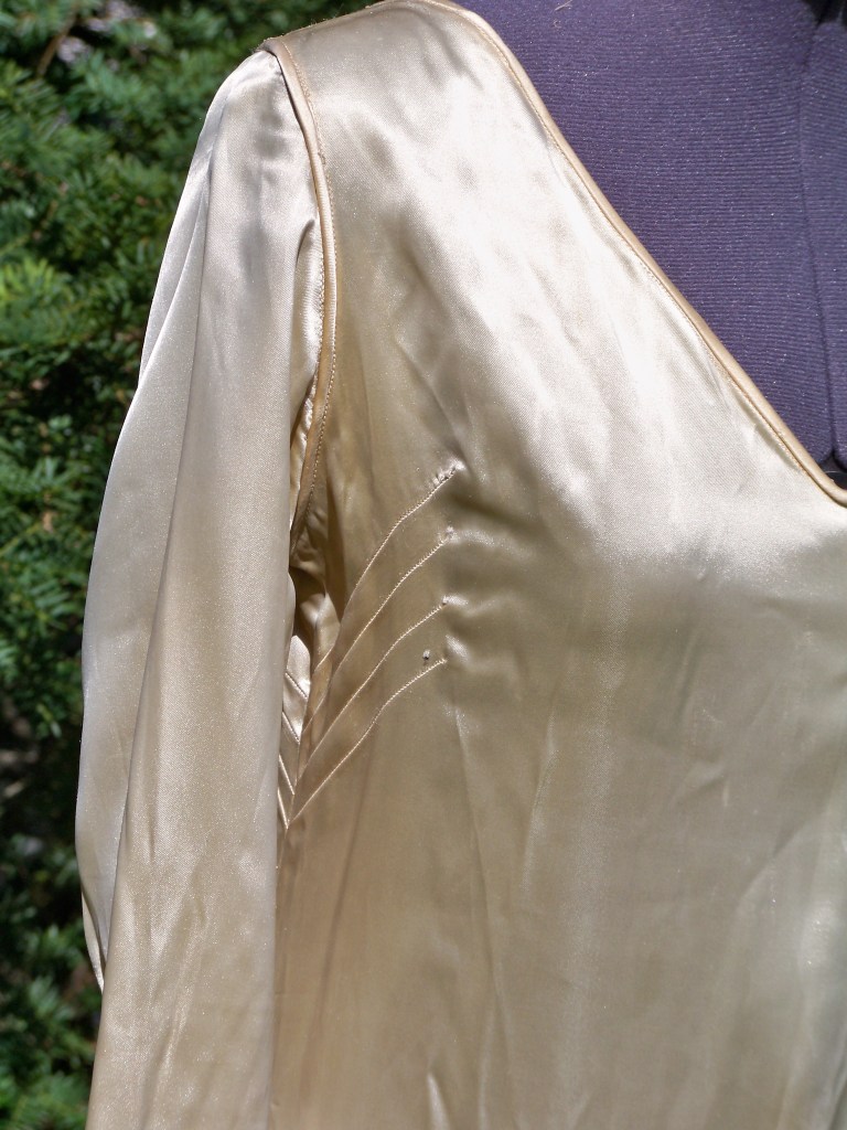 Close up photo of front of cream satin wedding dress showing the three diagonal tucks on the side of the top near the bust line.