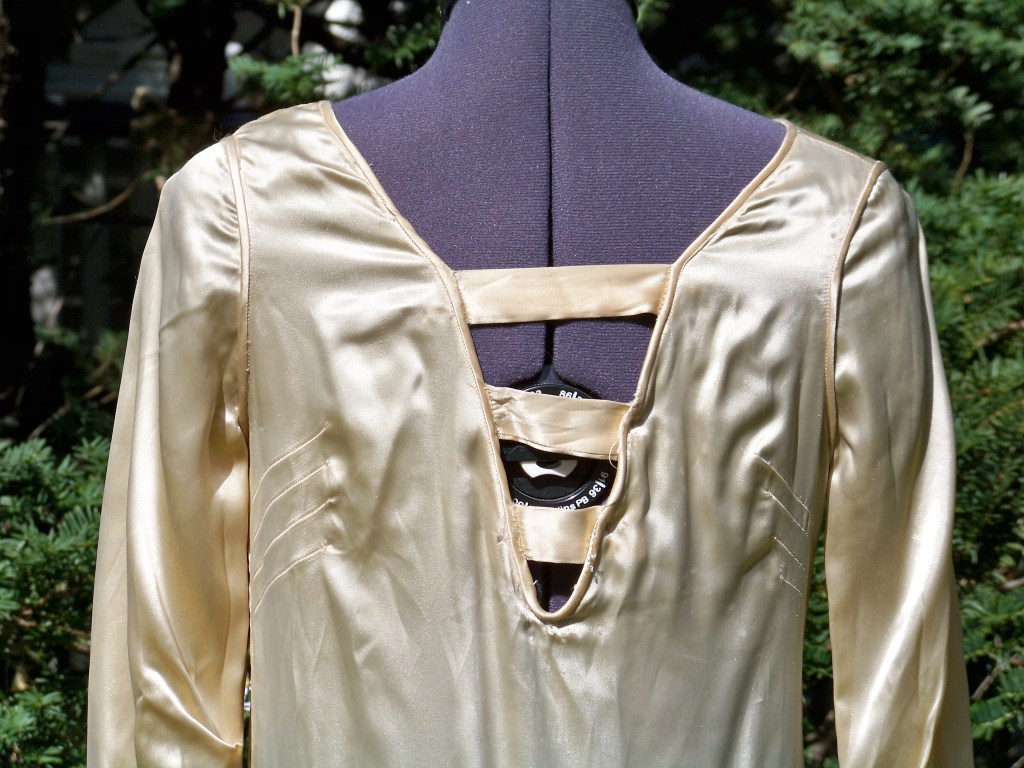 Close up of back of cream satin wedding gown with three horizontal fabric strips sewed across the deep V neckline.