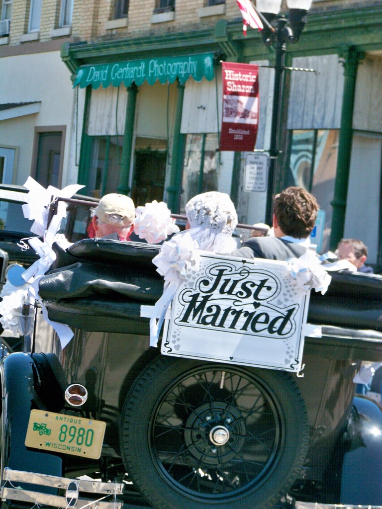 Model A Ford convertible with Just Married sign on back driving off with Bride and Groom in back seat.