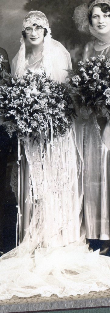 Bride in long satin sleeveless dress with scooped neckline and large bouquet of roses.