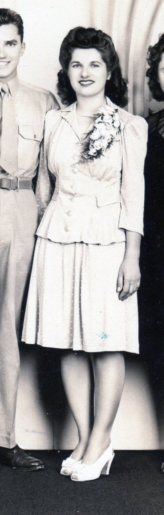 Bride wearing a two piece dress with knee-length skirt instead of a bridal gown and veil, and wearing a large corsage instead of a bridal bouquet.