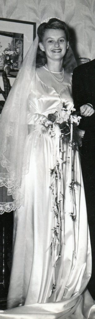 Picture of just the Bride in her shiny satin dress and bouquet of flowers with white ribbons hanging down, greenery tied on.