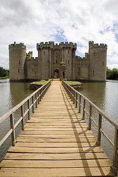 View of a castle in a lake that is reached by a wooden bridge. The bridge starts at the center bottom of the photo and stretches to the door of the castle.